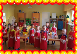 Na zdjęciu grupa dzieci w czerwonych fartuchach.